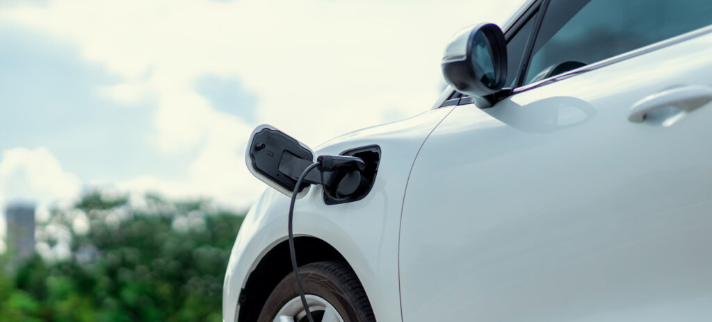 Focus closeup electric vehicle plugged in with EV charger device from blurred background of public charging station powered by renewable clean energy for progressive eco-friendly car concept.